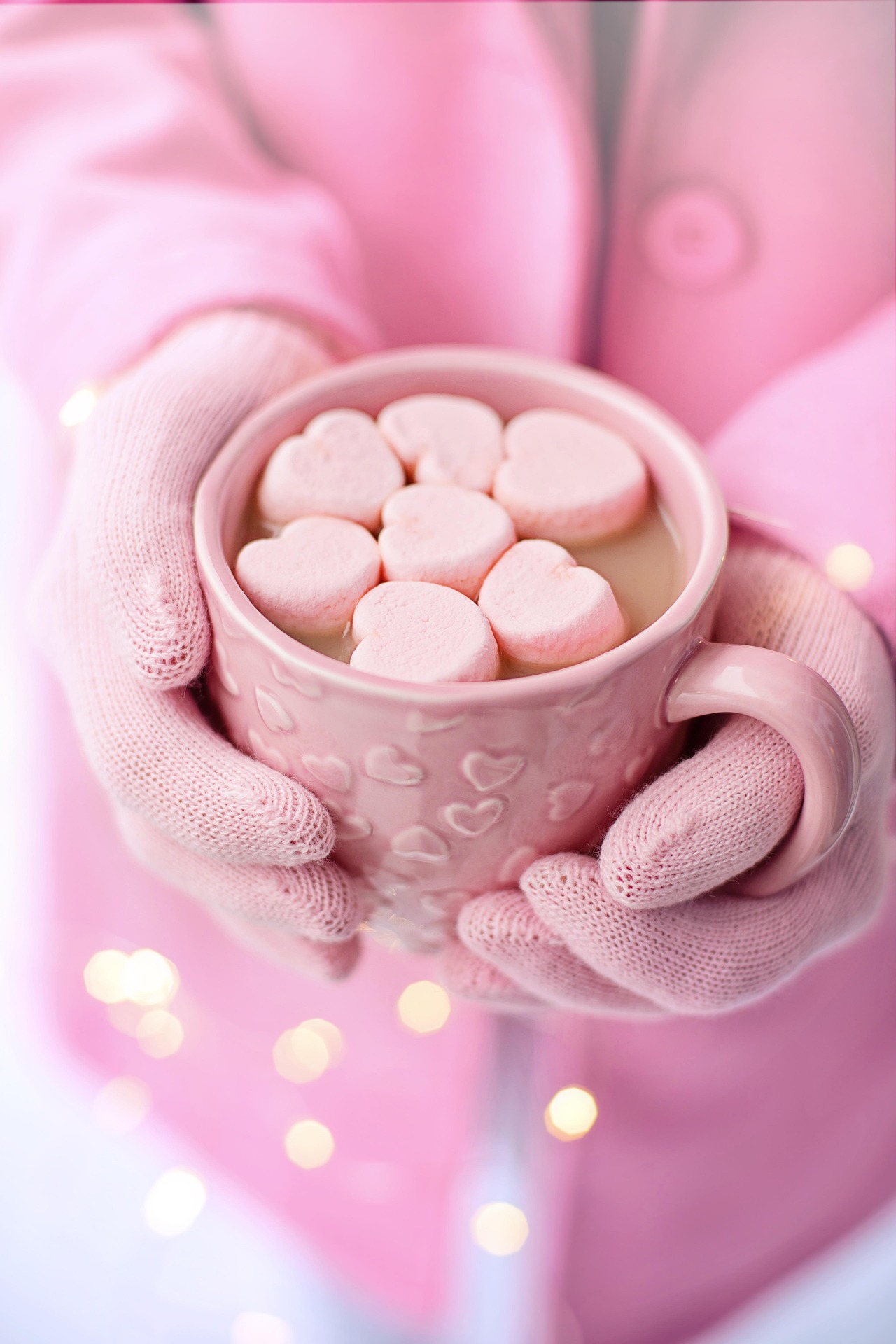 Pink hands holding a pink mug of hot chocolate with heart shaped marshmallows